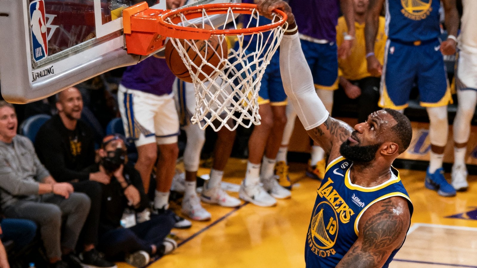 NBA湖人队对阵勇士队比赛集锦封面，詹姆斯在第三节完成一记势大力沉的隔人暴扣，篮筐震颤，替补席球员集体起立欢呼。